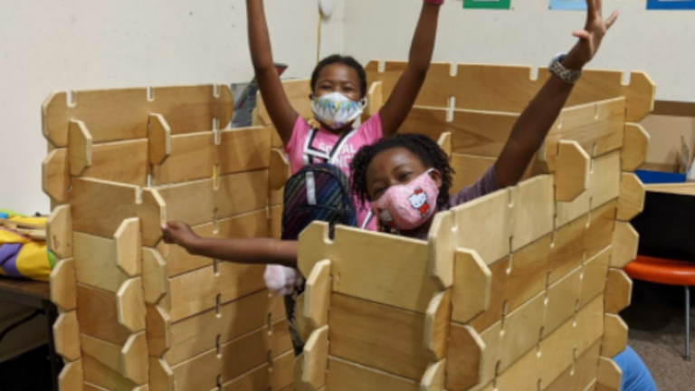 Two children in a wooden fort made in the library's makerspace