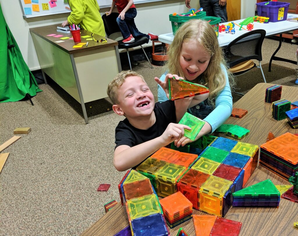 Two children laugh while building with magnatiles