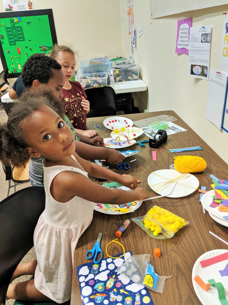 A child builds a pinball game out of a paper plate and other craft supplies