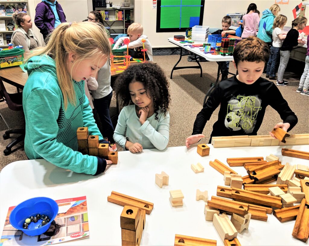 Three children are focused on building a wooden marble run