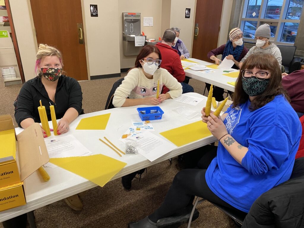 Three people sit at a table with candlemaking supplies and beeswax candles
